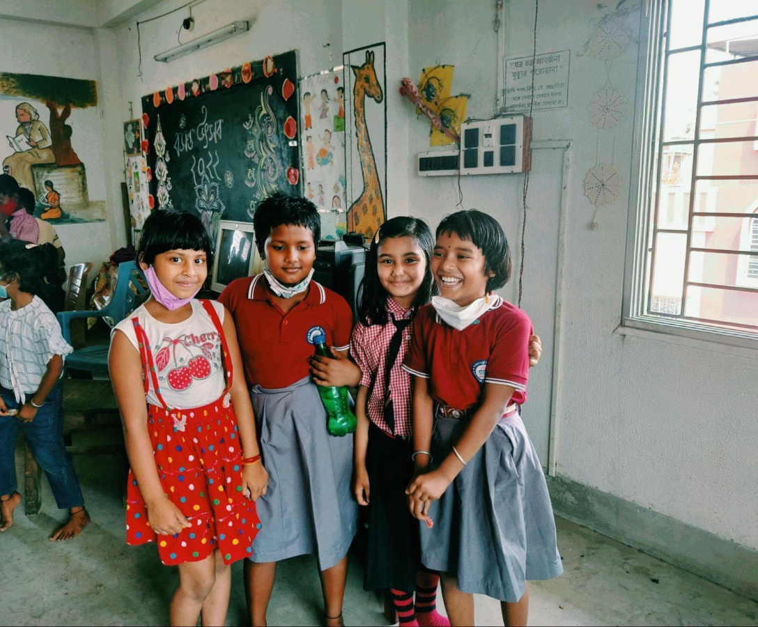 Four children standing together and smiling in a classroom
