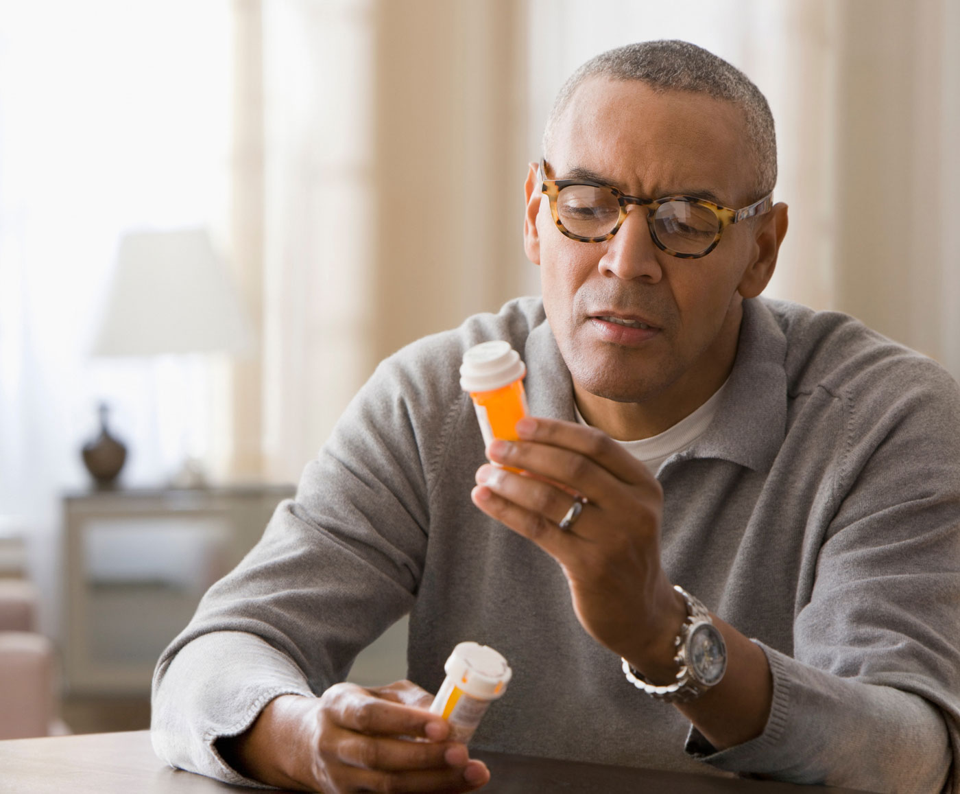A man sitting at a table reads the label on a pill bottle