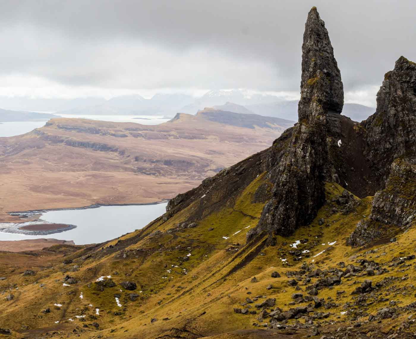 A close up of the edge of a mountain with lakes and more mountains in the distance