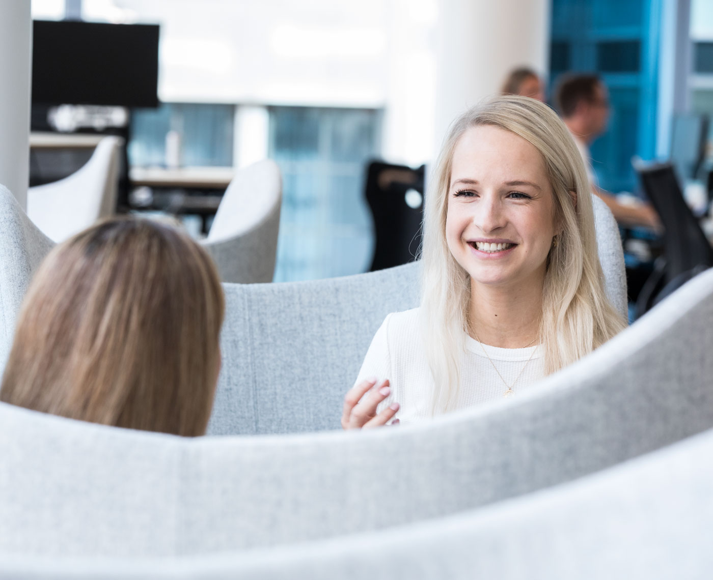 Two women having a conversation and smiling sit in a booth in an office breakout area