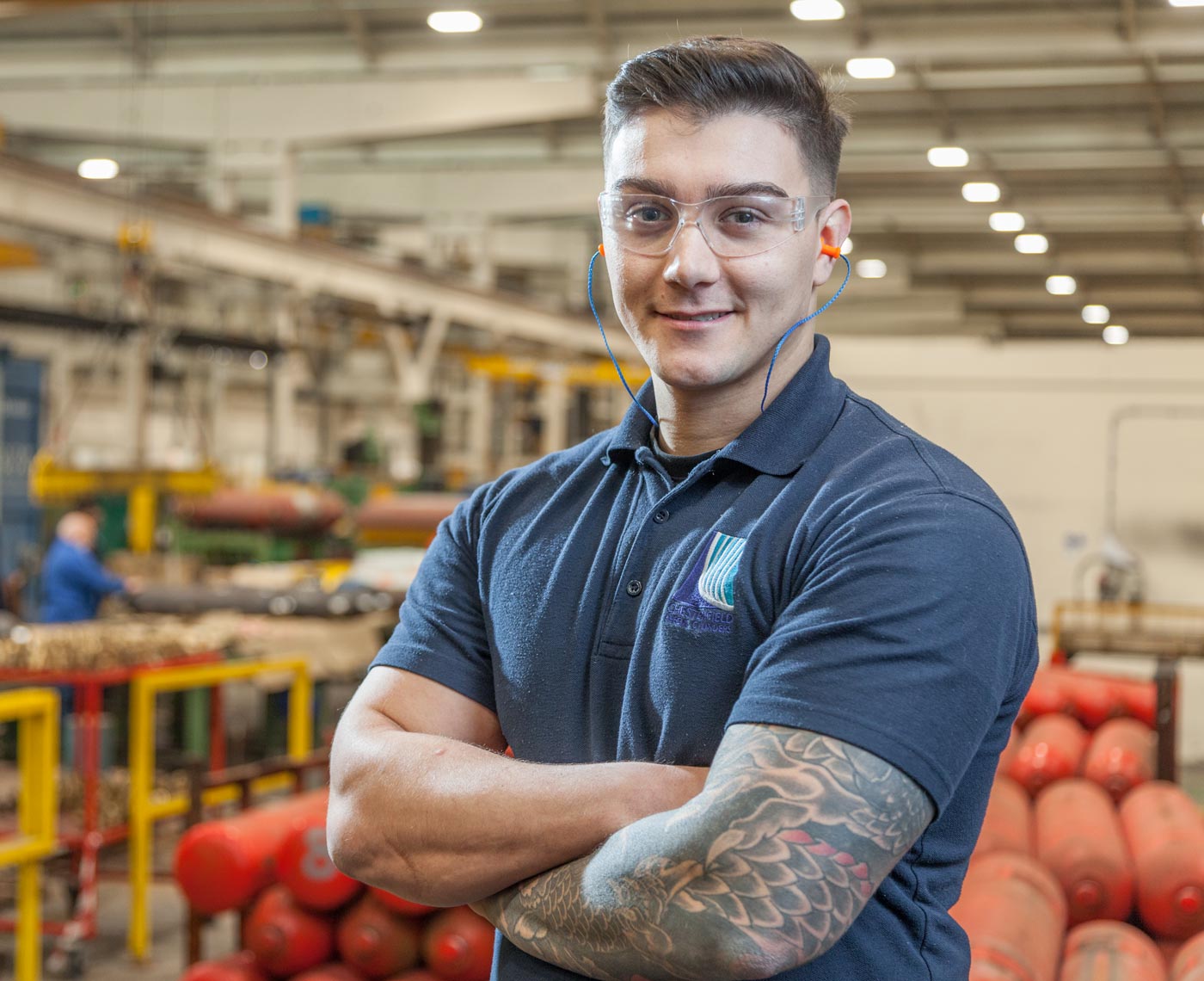 A man stands looking at camera wearing safety equipment in a factory setting