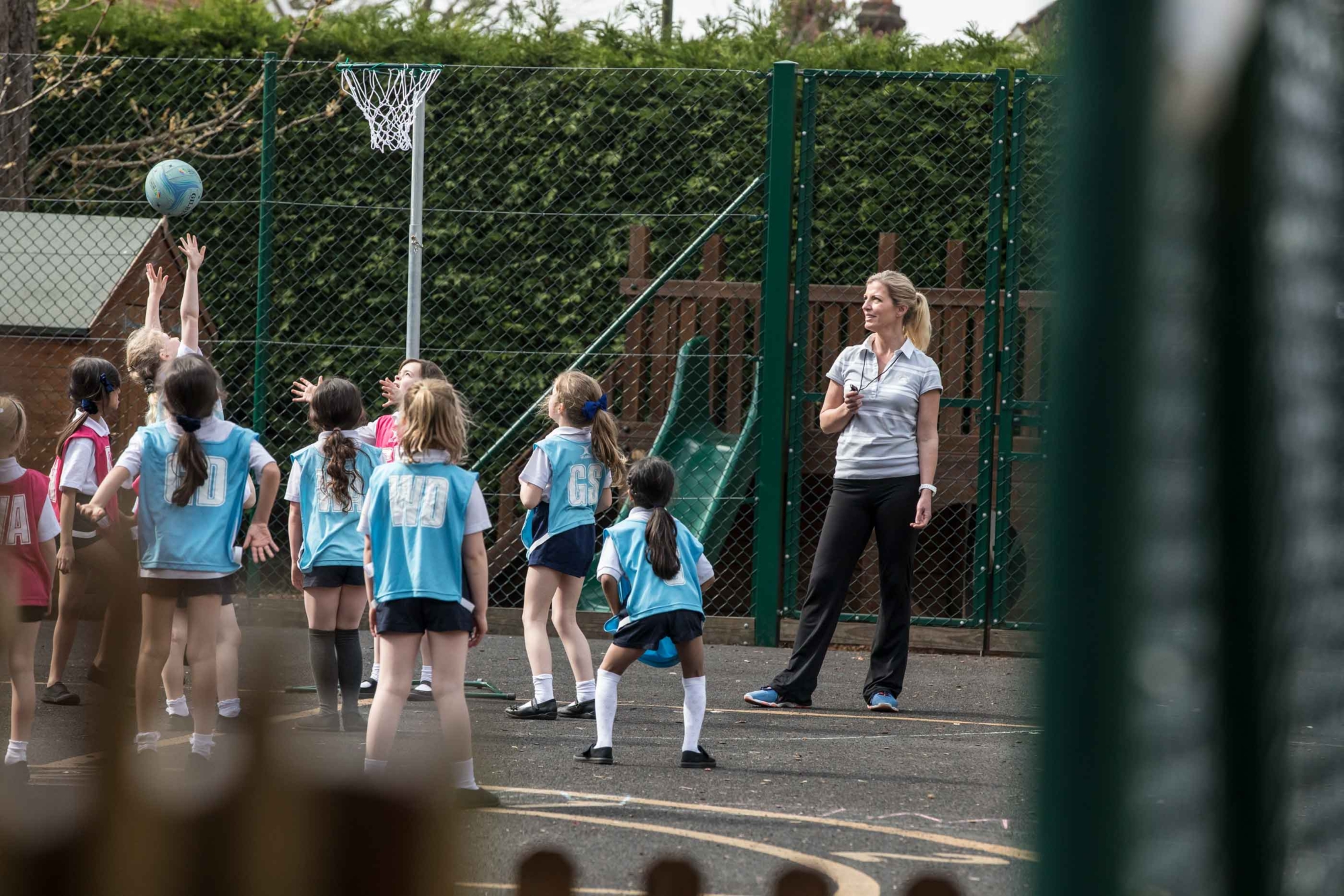 A PE teacher instructs a group of young pupils in netball