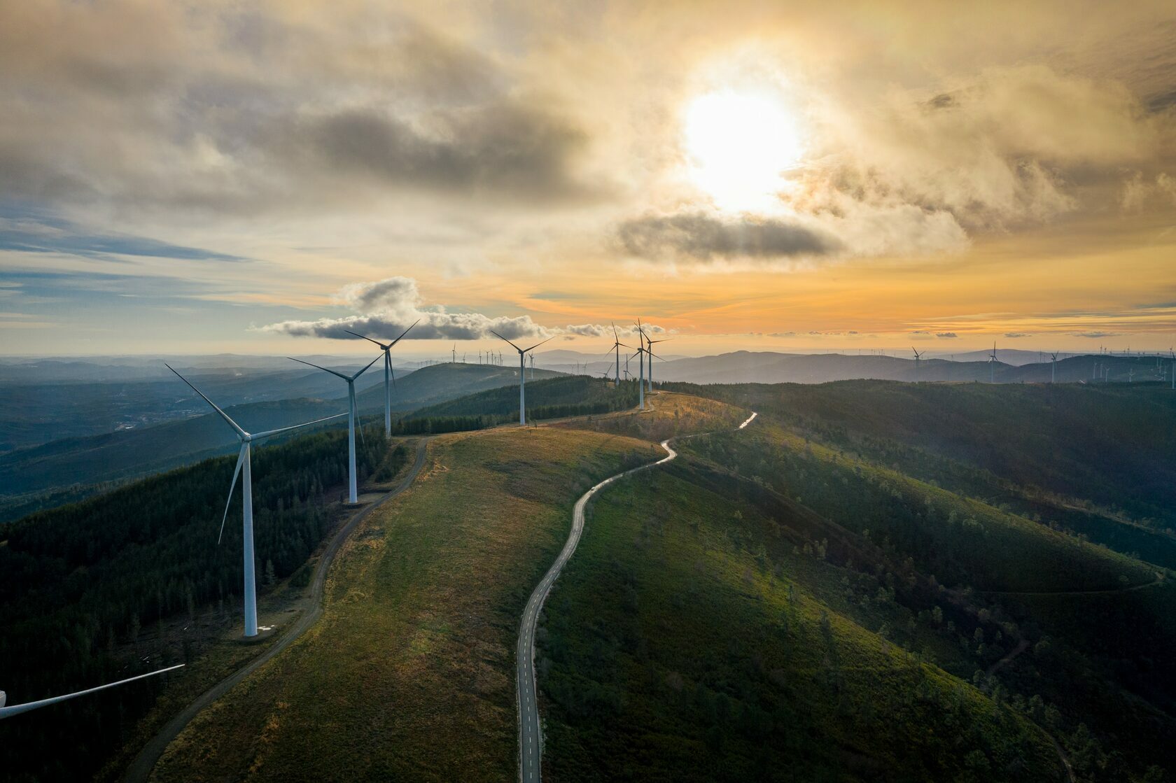A hilly landscape in late afternoon sun with wind farms and ocean in the distance